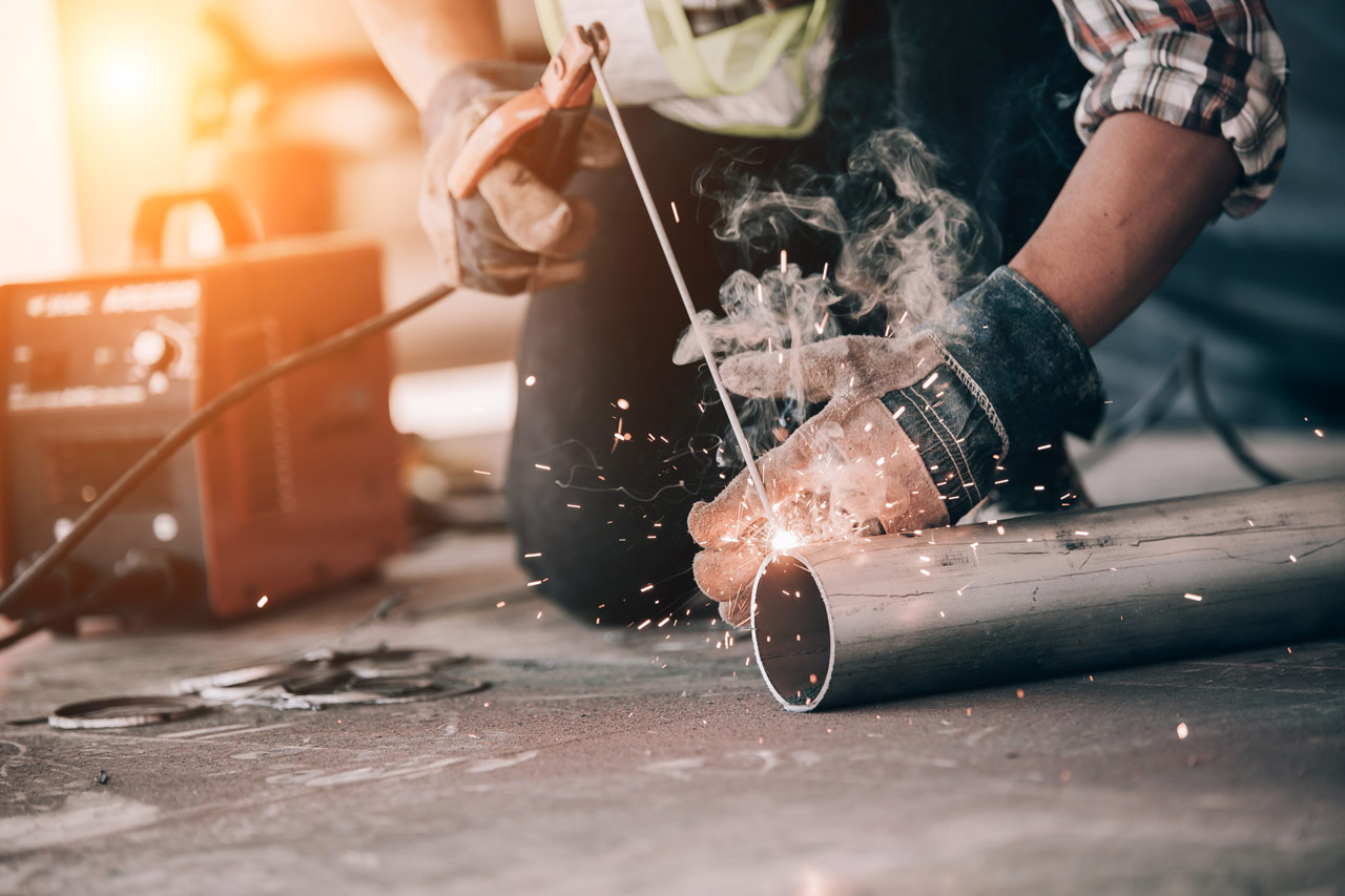 close up of a welder wearing a protective glove and a mask welding metal with sparks